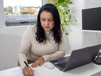 Veronica Cardoso fazendo anotações em sua mesa de atendimento, ao lado do notebook