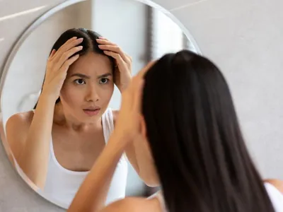 Mulher examinando a raiz do cabelo diante do espelho