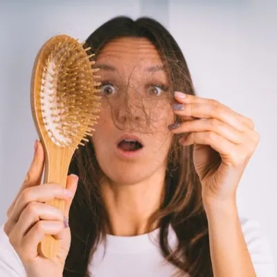 Mulher assustada segurando uma escova cheia de fios de cabelo caídos