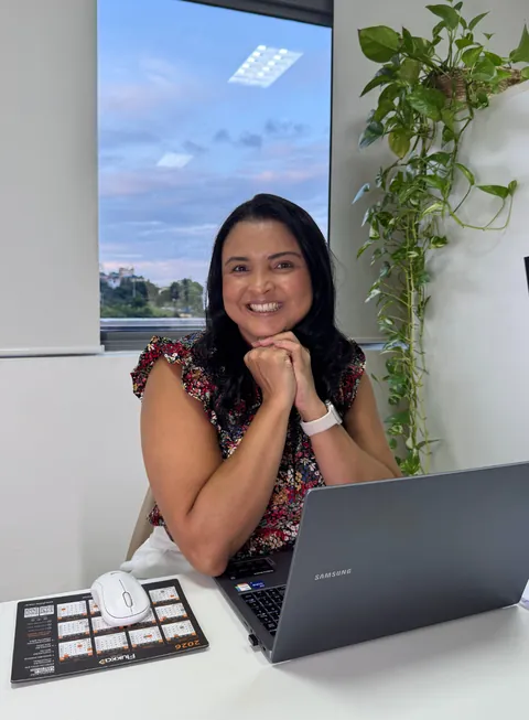 Veronica Cardoso sorrindo em sua mesa de atendimento, com o notebook aberto